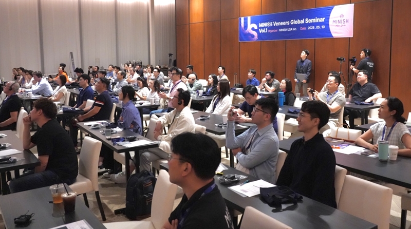 A large group of attendees participating in the MINISH Veneers Global Seminar, seated at tables with microphones and recording devices, engaged in a presentation.